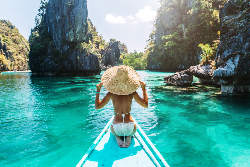 Back view of a young woman in straw hat relaxing on the boat and looking forward into lagoon. Travelling tour in Asia: El Nido, Palawan, Philippines.