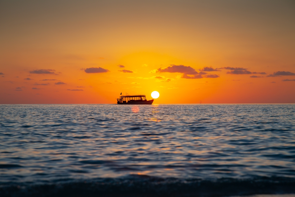 Tourist boat on horizon line close to the Sun at sunset in Maldives