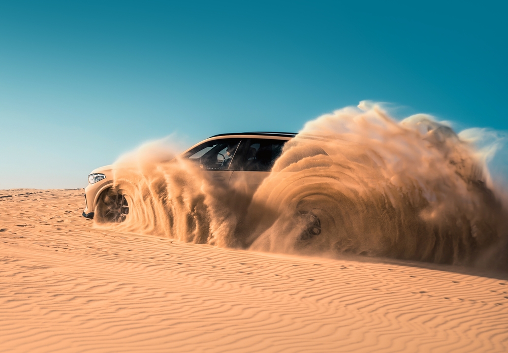 Brand new SUV BMW X5 in the desert climbing sand dune splashing sands around