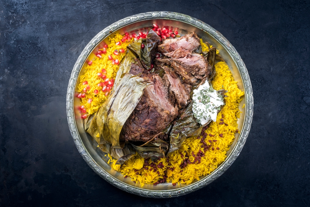 Slow cooked Omani lamb shuwa coated in rub of spices and wrapped in banana leaves served with rice and yoghurt as top view on a rustic oriental tray