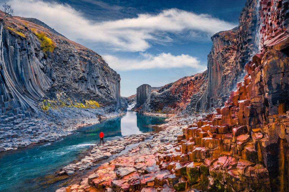 Tourist walking on the bottom of canyon with basalt columns. Unbelievable summer scene of Studlagil Canyon.