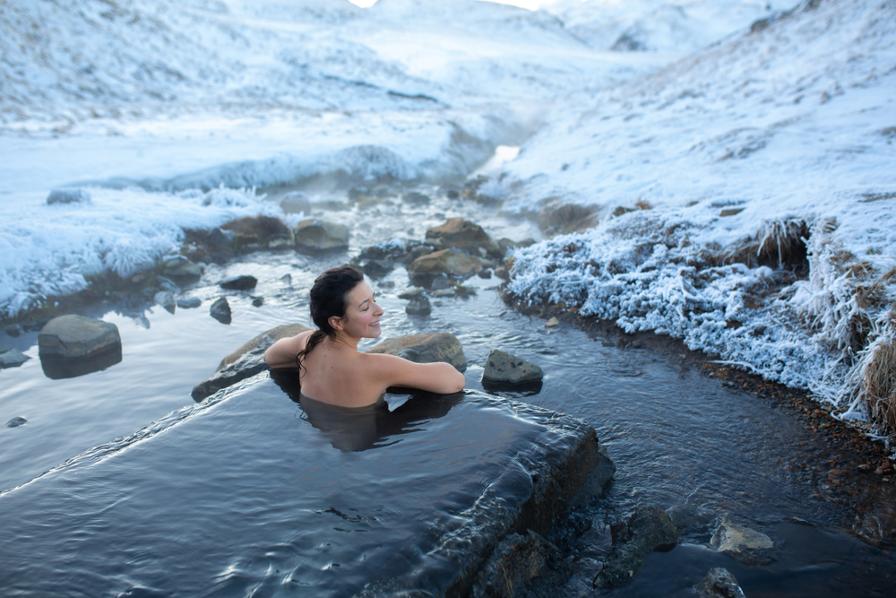 The girl bathes in a hot spring in the open air with a gorgeous view of the snowy mountains. Incredible iceland in winter.