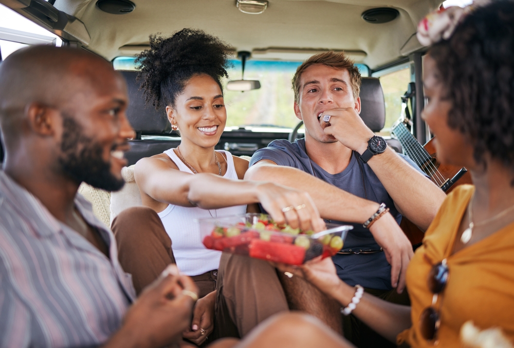 Diversity, food and friends on road trip with fruit while on holiday vacation eating watermelon, grapes and strawberry.