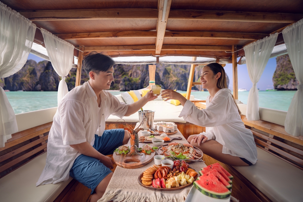 Asian couple lover travel and relax in they honeymoon trip on the wooded boat and eat seafood togather at Koh phi phi island, Maya beach, Phang nga near Phuket in Thailand