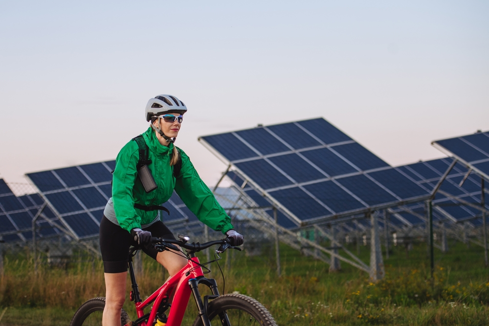 Portrait of a beautiful cyclist riding in front of solar panels at a solar farm.