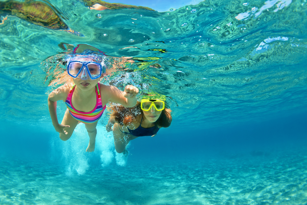 Happy family - mother with baby girl dive underwater with fun in sea pool.