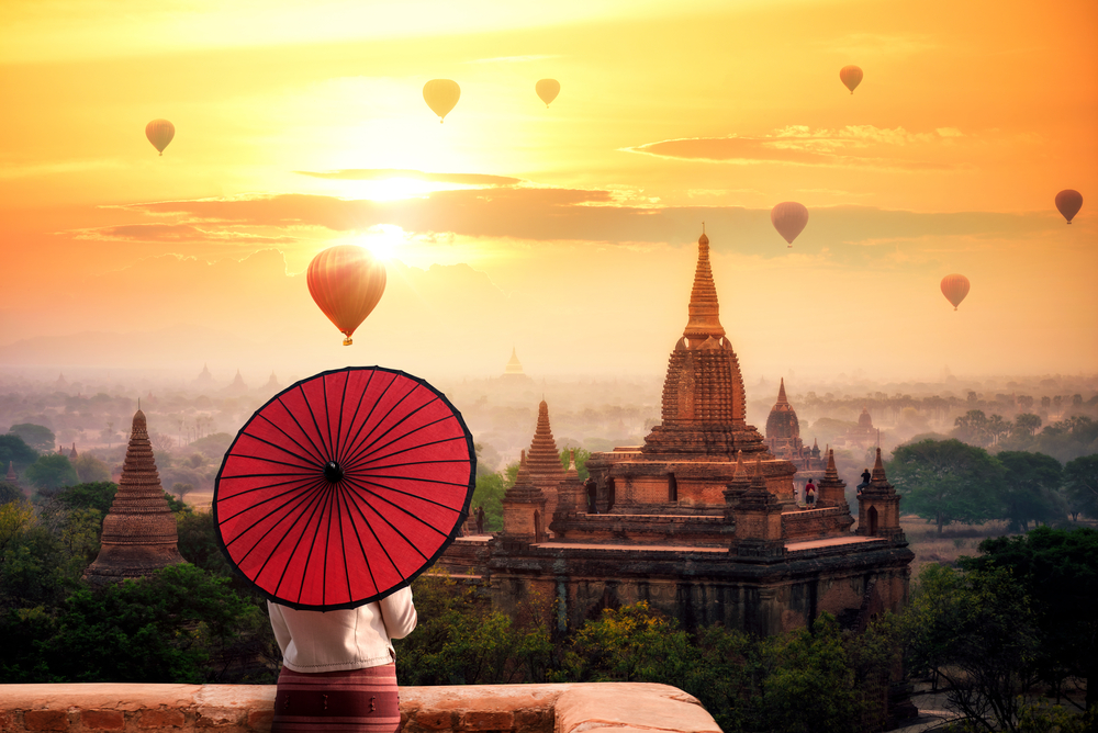 Unidentified Burmese woman holding traditional red umbrella and looks at Hot air balloon over plain of Bagan in misty morning, Mandalay, Myanmar