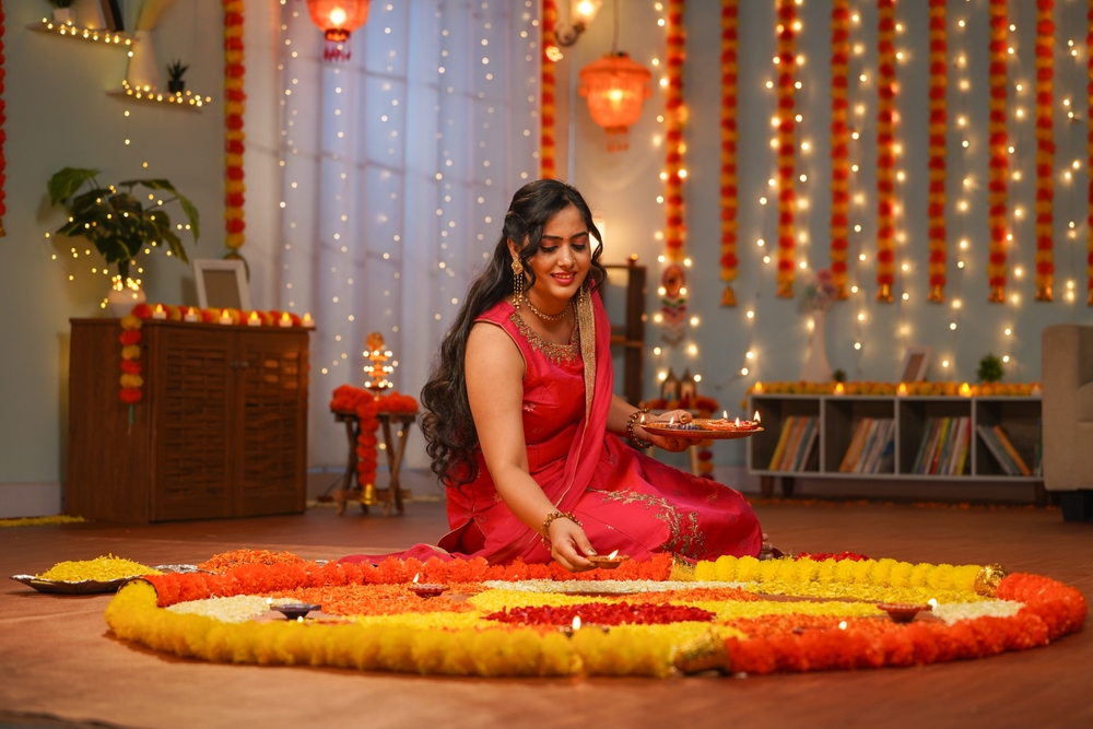 Happy young Indian woman placing diya lamps on decorated flower rangoli for diwali festival celebration at home