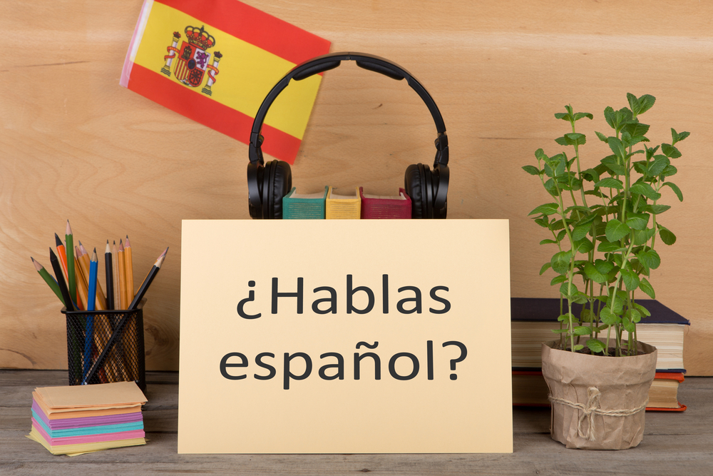 Concept of learning the spanish language - paper with text "¿hablas español?" (hablas espanol), flag of the Spain, books, headphones, pencils on wooden background