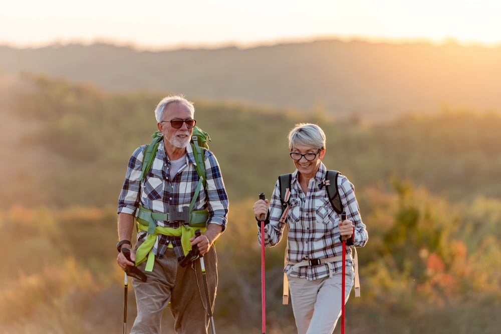 Active senior Caucasian couple hiking in mountains with backpacks and hiking poles, enjoying their adventure