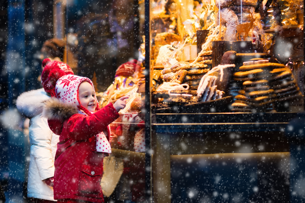 Children window shopping on traditional Christmas market in Germany on snowy winter day. 