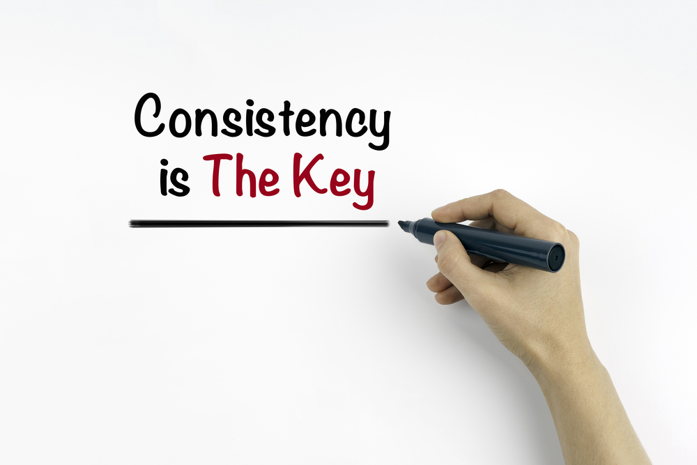 Hand with marker writing: Consistency is The Key