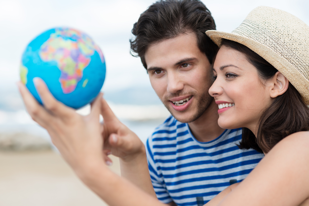 Excited young couple planning their holiday holding up a globe and pointing to a travel destination with focus to the attractive woman in a trendy straw hat