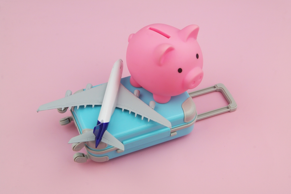 Travel budget concept. Pink piggy bank with airplane model on suitcase on pink background