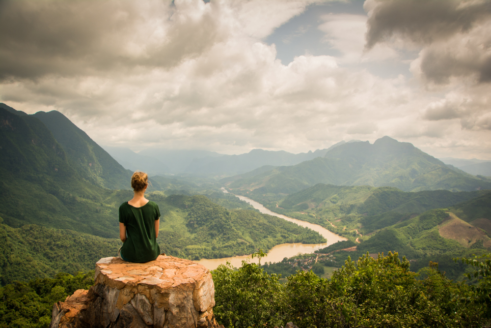 Girl with green shirt sitting on a rock on top of a mountain watching the beautiful scenery of the backcountry of Nong Khiaw, Laos.