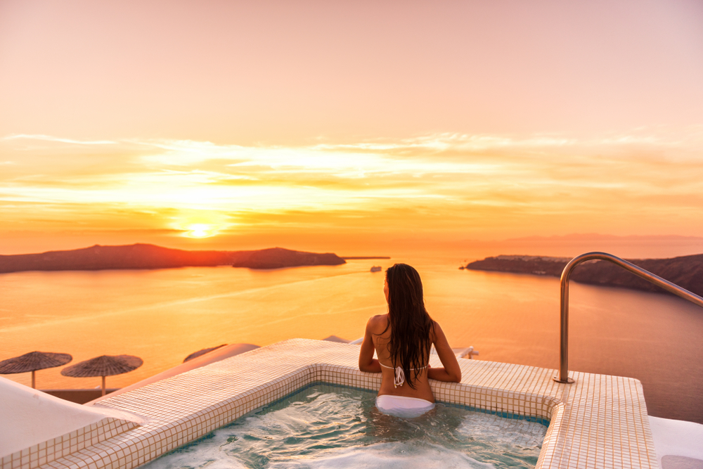 Luxury travel Santorini vacation woman swimming in hotel jacuzzi pool watching sunset.