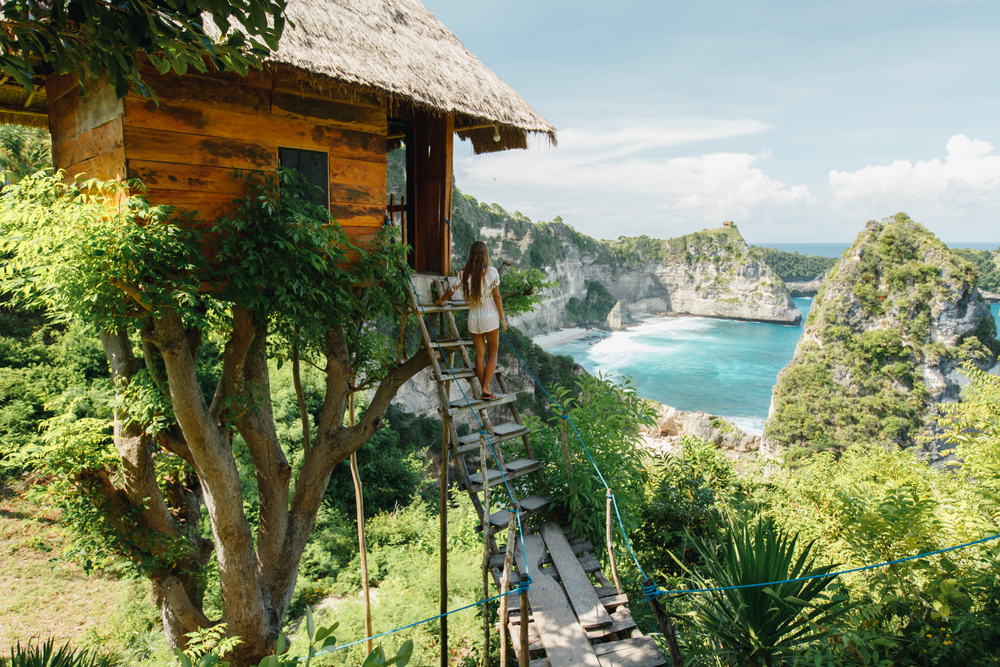 Young girl on steps of traditional house on tree, look at Atun beach, Nusa Penida island.