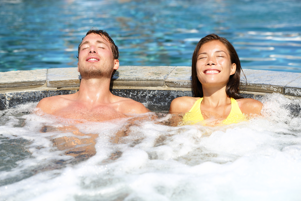 Spa couple relaxing enjoying jacuzzi hot tub bubble bath outdoors on romantic summer vacation travel holidays or honeymoon.