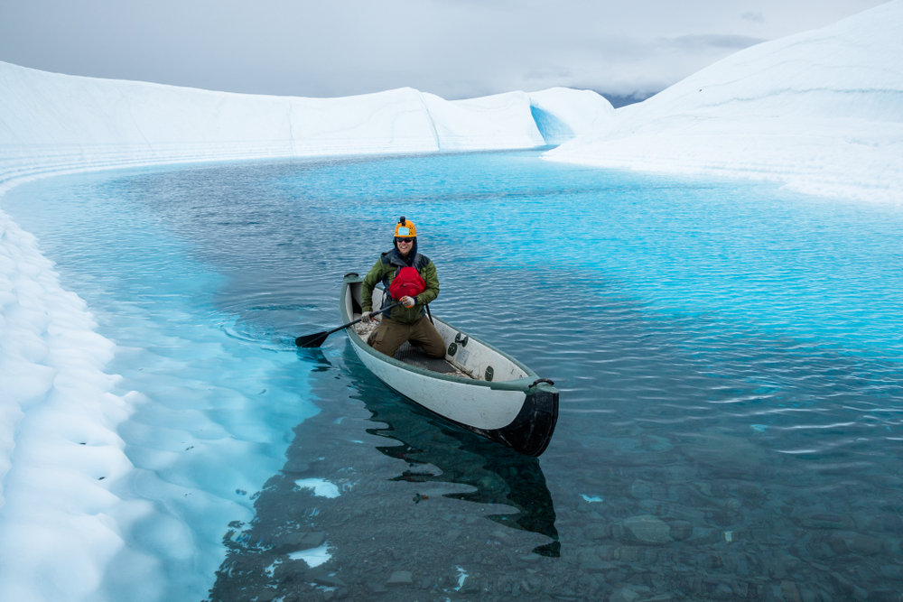 On a lake on top of the Matanuska Glacier, a young man paddles to a shallow section with rocks to land his canoe.