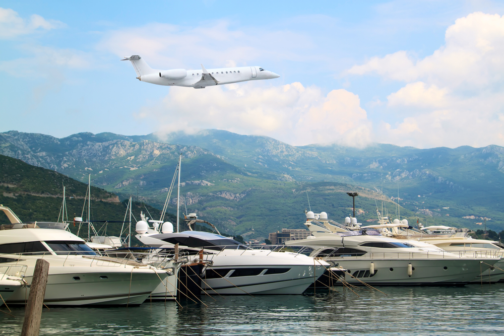 Private jet business plane flies low over yachts and boats in gulf of background of mountains with white clouds