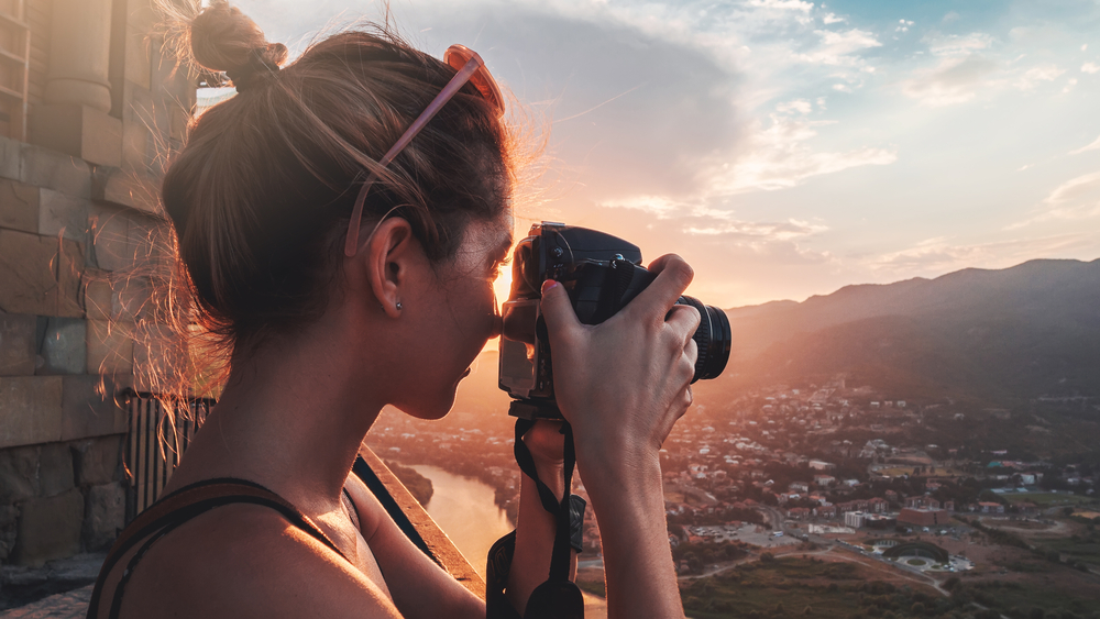 Female photographer, taking pictures of mountain landscape at sunset in Georgia