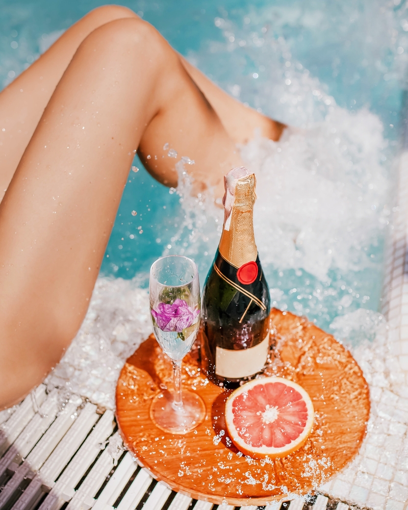 glass of champagne, bottle, grapefruit by the pool. splashes and female legs. cocktail summer party.