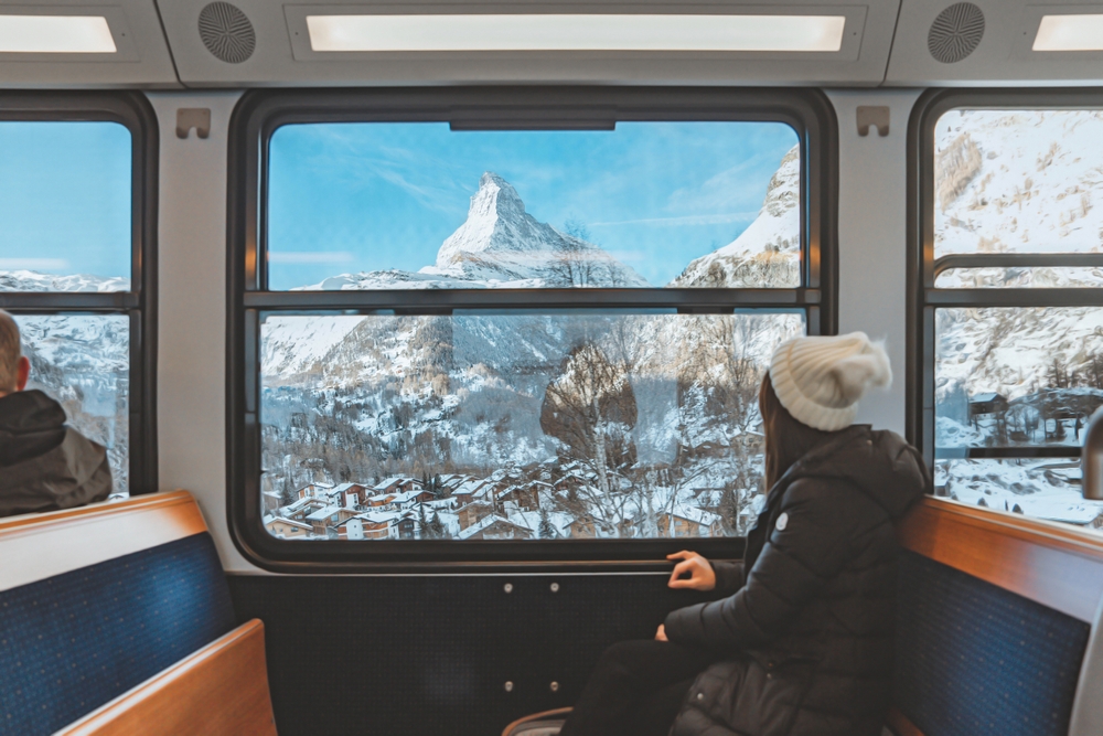 young woman traveling looking out the window enjoying in Swiss Alps with the Matterhorn in winter background while sitting in the train.