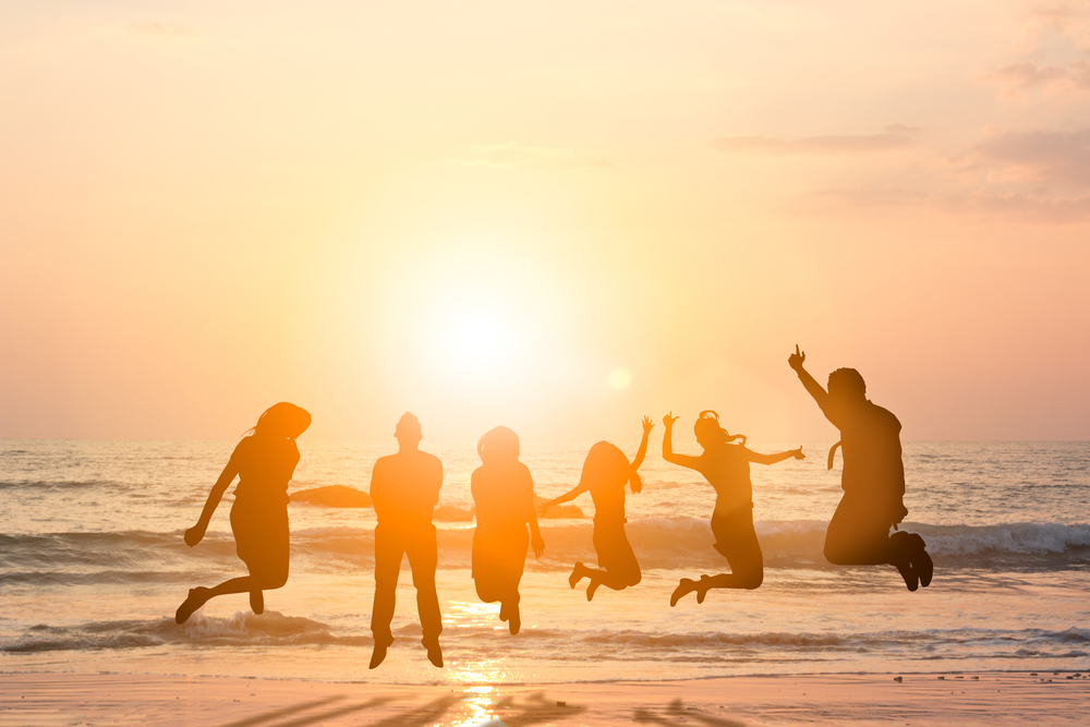 Silhouette friends jumping with joy and happiness over blurred, sand and sea.