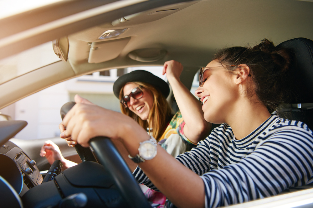 Two trendy attractive young woman singing along to the music as they drive along in the car