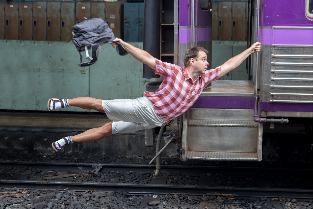 Man with backpack flies behind a moving train. Tourist holding a moving train from a railway station. 