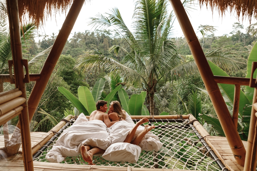 Happy travel couple on hammock balcony of bamboo tree house with jungle nature view.