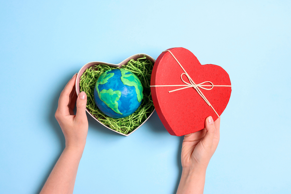 Female hands holding heart gift box with planet earth on a blue background.