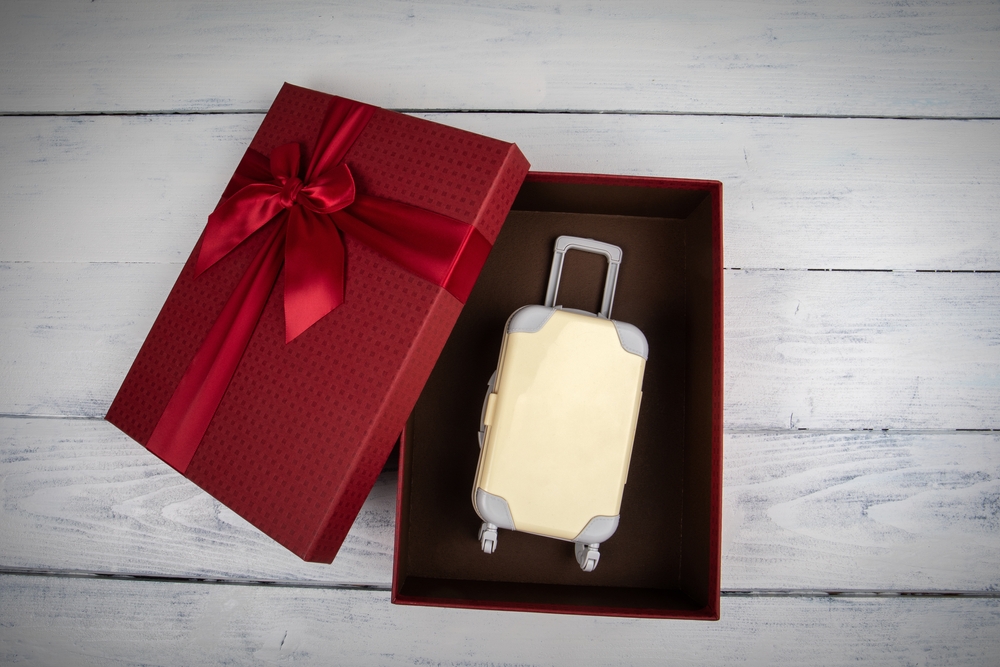 Trip as a gift concept. red gift box with miniature travel suitcase.