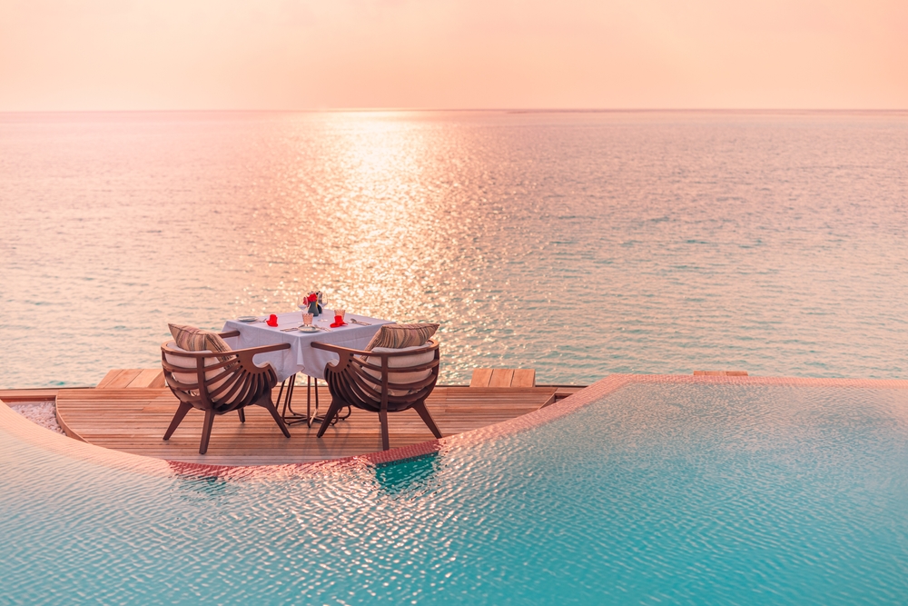 Seascape view under sunset light with dining table with infinity pool around.