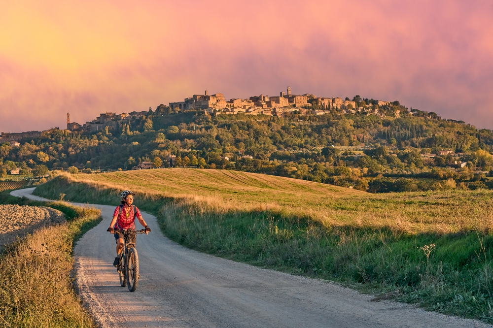 nice senior woman riding her electric mountain bike between olive trees in the Ghianti area with Montepulciano in background, Tuscany , Italy