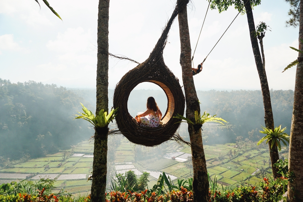 A young woman tourist sitting in a bird nest, immersed in the breathtaking green landscape of Bali on a sunny day. 
