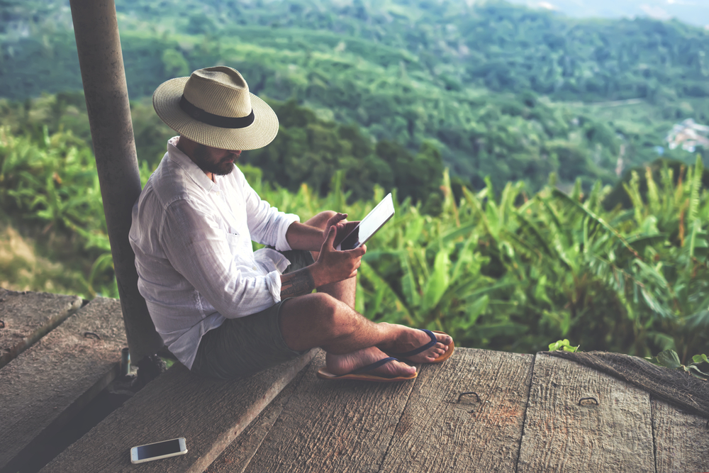Man traveler is using digital tablet, while is sitting against beautiful Asian scenery during summer journey.