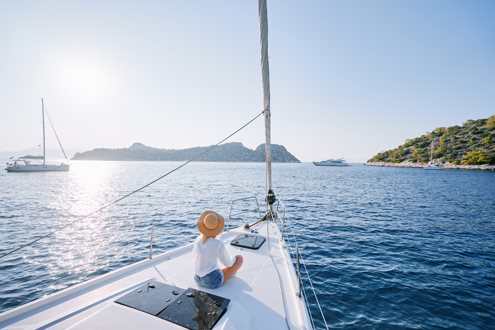 Luxury travel on the yacht. Young happy woman on boat deck sailing the sea. Yachting in Greece.