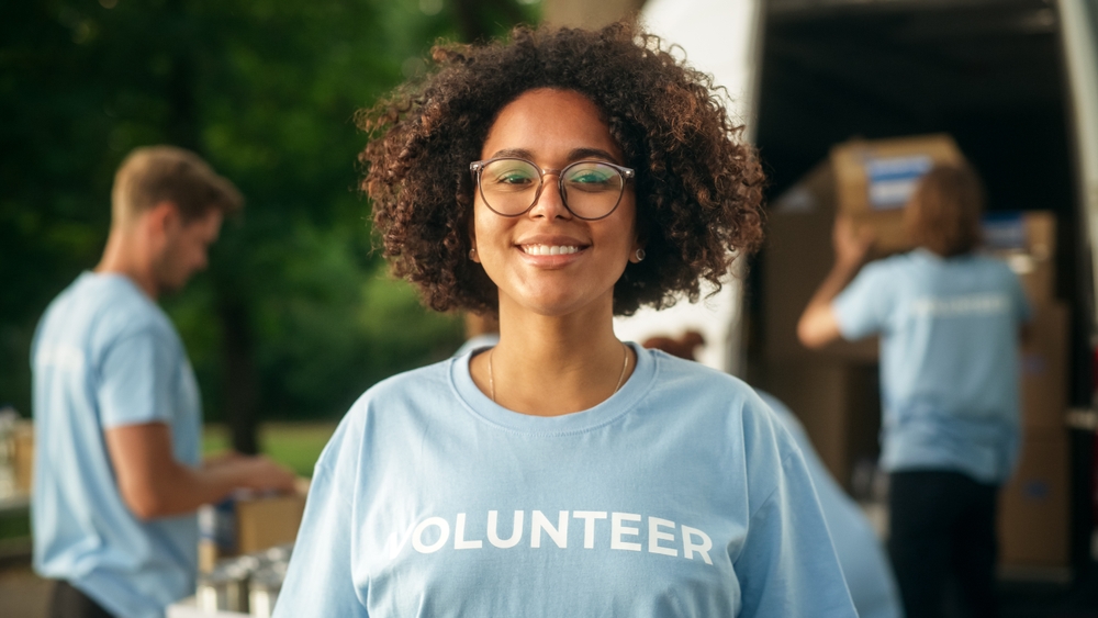 Portrait of a Happy Helpful Black Female Volunteer. Young Adult Multiethnic Latina with Afro Hair, Wearing Glasses, Smiling, Posing for Camera. Humanitarian Aid and Volunteering Concept.