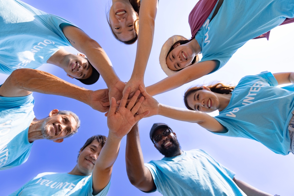 Team of young and diversity volunteer worker group enjoy charitable social work outdoor together in saving environment project wearing blue t-shirt while joining hand in power assemble unity