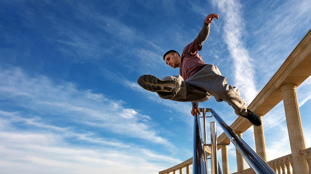 Sport man practicing parkour in urban space. Parkour athlete jumping on stairs over the railing. Free runner have workout city street.