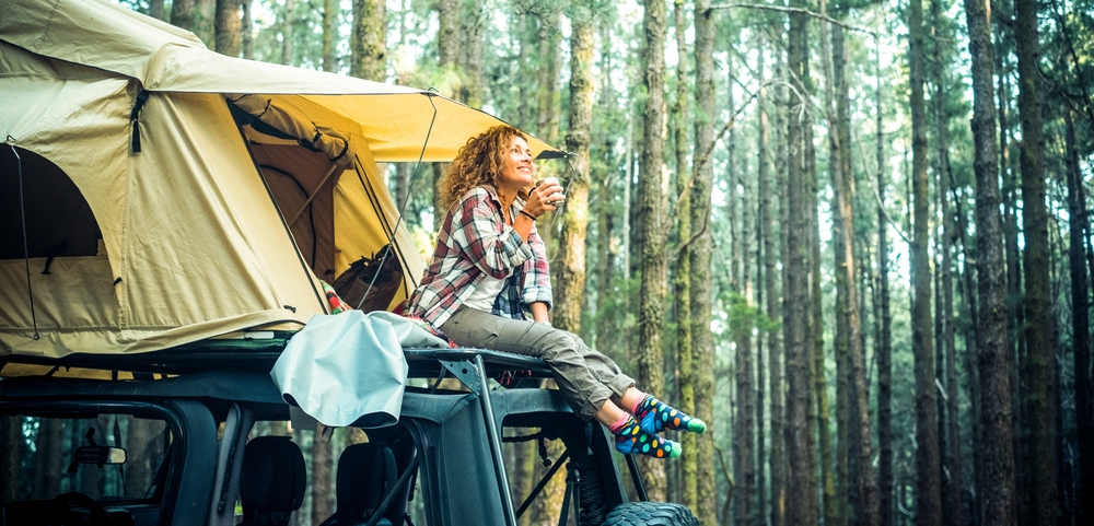 Freedom feeling and adventure lifestyle people. Traveler adult female chilling outside her car vehicle roof tent and enjoy nature sounds smiling.