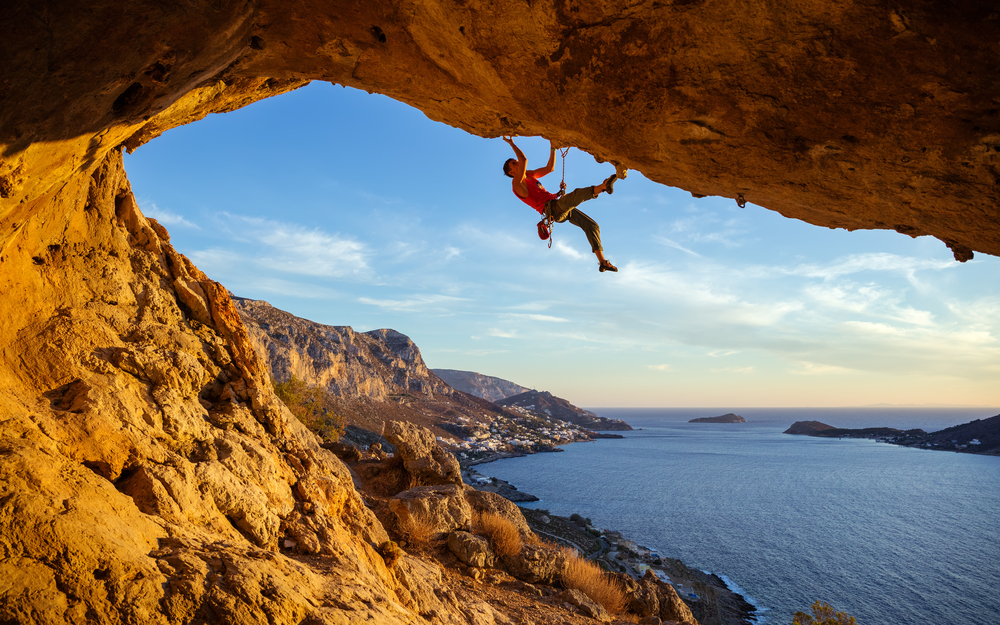 Male climber on overhanging rock against beautiful view of coast below