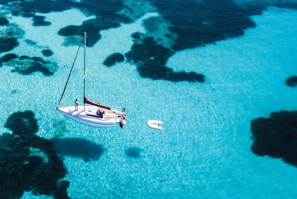 Aerial view of a sail boat in front of Mortorio island in Sardinia. Amazing beach with a turquoise and transparent sea. Emerald Coast, Sardinia, Italy.