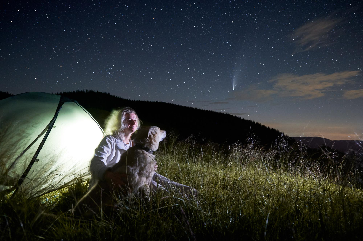 Young woman in the mountains observing beautiful starry night and a comet