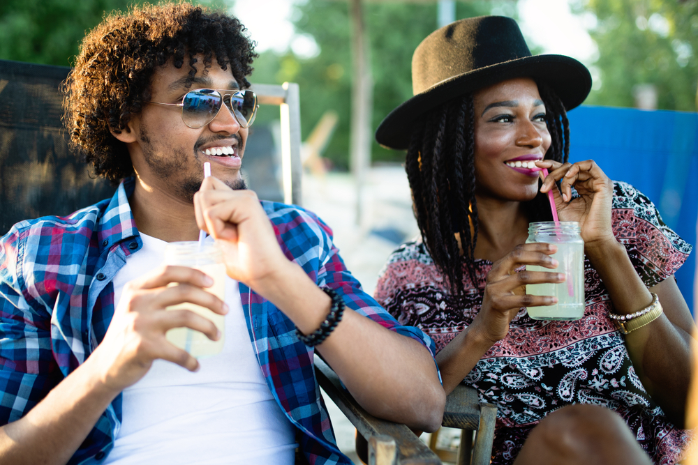 Young happy black couple with drinks relaxing on the beach