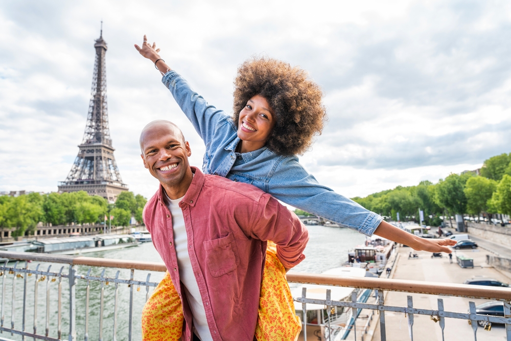 Black cheerful happy couple in love visiting Paris city centre and Eiffel Tower - African american tourists travelling in Europe and dating outdoors