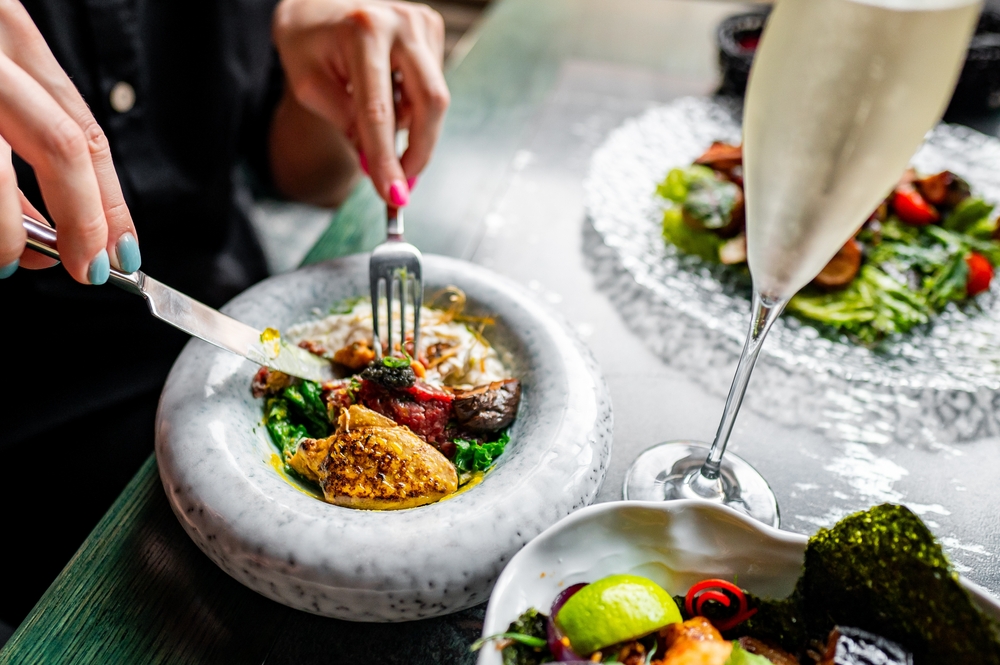 A person dining at a restaurant, enjoying a colorful gourmet dish served on a unique marble plate, capturing the fine dining experience