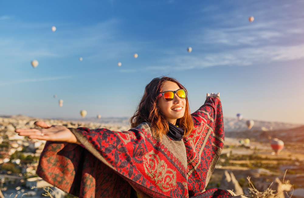 A tourist girl on a mountain top enjoying wonderful view of the sunrise and balloons in Cappadocia. Happy Travel in Turkey concept