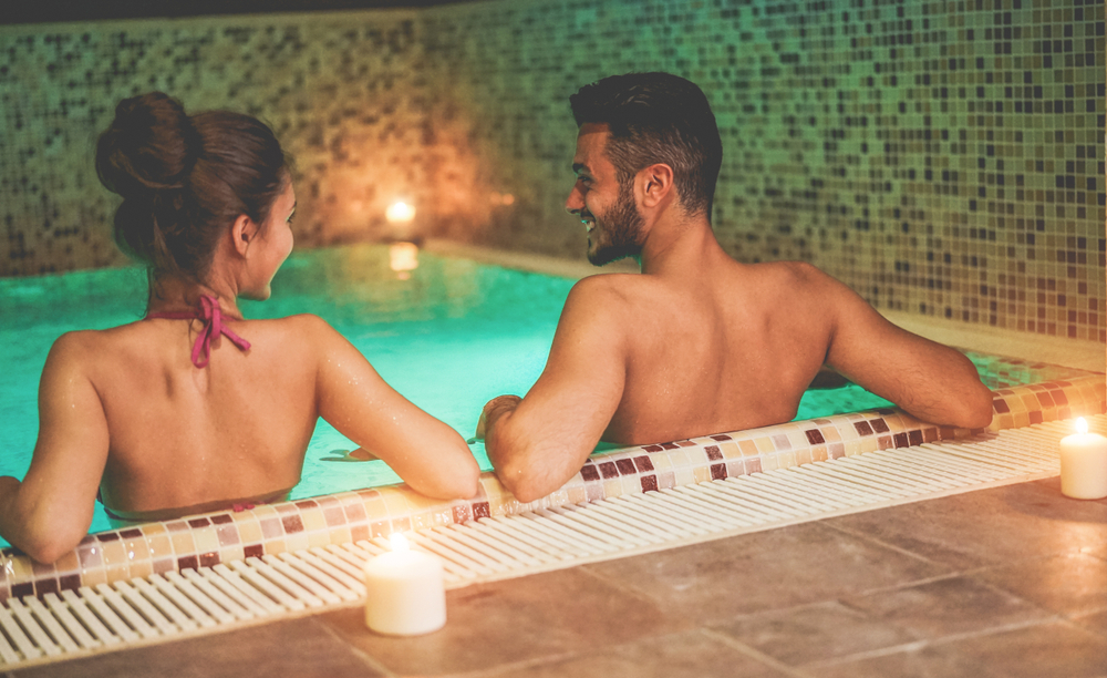 Happy couple enjoying spa swimming pool with candles and soft lights - Young people doing romantic vacation in resort hotel - Relationship, holidays and love concept - Focus on woman head